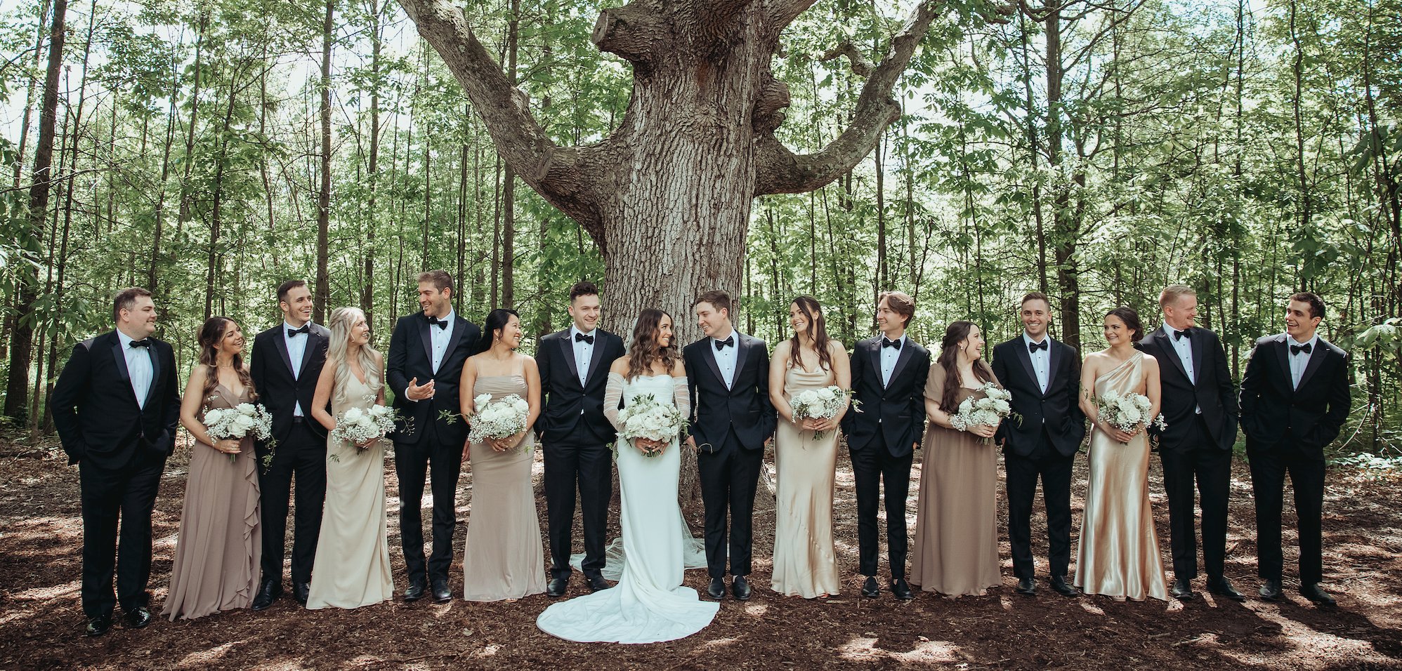 Bride and groom with wedding party under large tree at outdoor ceremony space, wooded backdrop at Retreat 21 near Columbus, Ohio