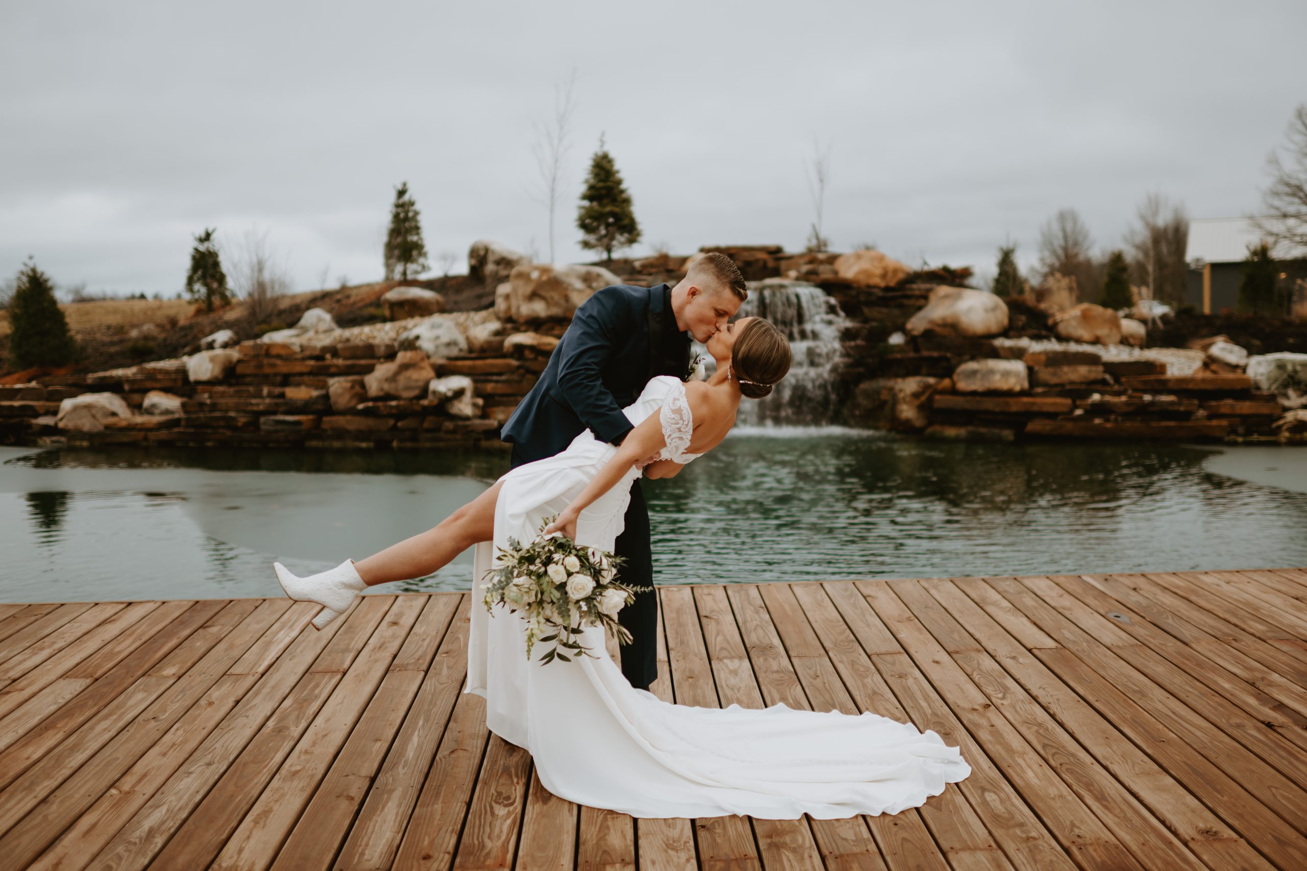 Groom dips and kisses bride in front of water feature at Retreat 21, romantic outdoor wedding moment near Columbus, Ohio
