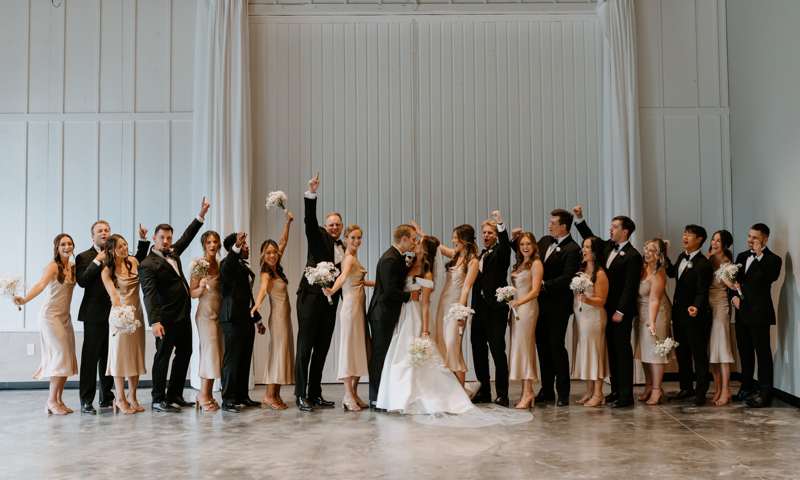 Bride and groom share a kiss indoors surrounded by their wedding parties at Retreat 21 near Columbus, Ohio