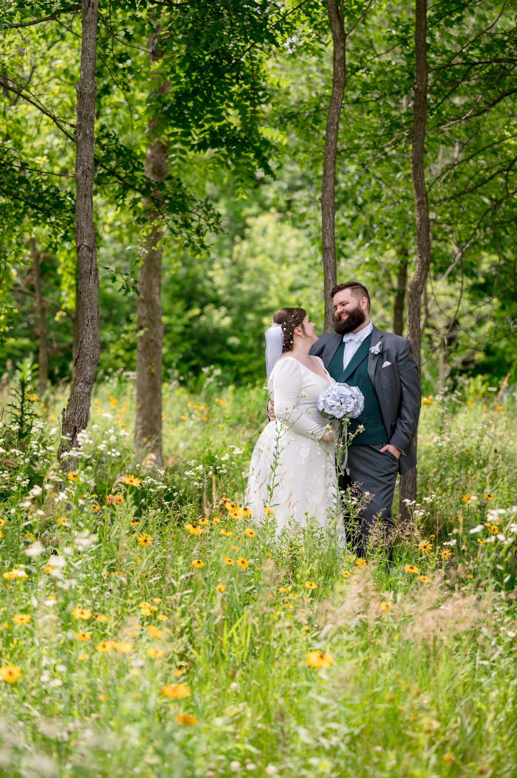 Bride and groom standing in tall grass surrounded by summer flowers and trees at Retreat 21 near Columbus, Ohio