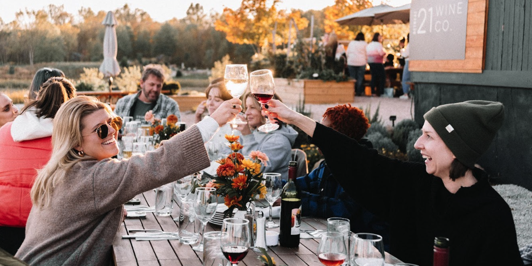 Guests sitting at a long outdoor table toasting during a fall wedding celebration at Retreat 21 near Columbus, Ohio