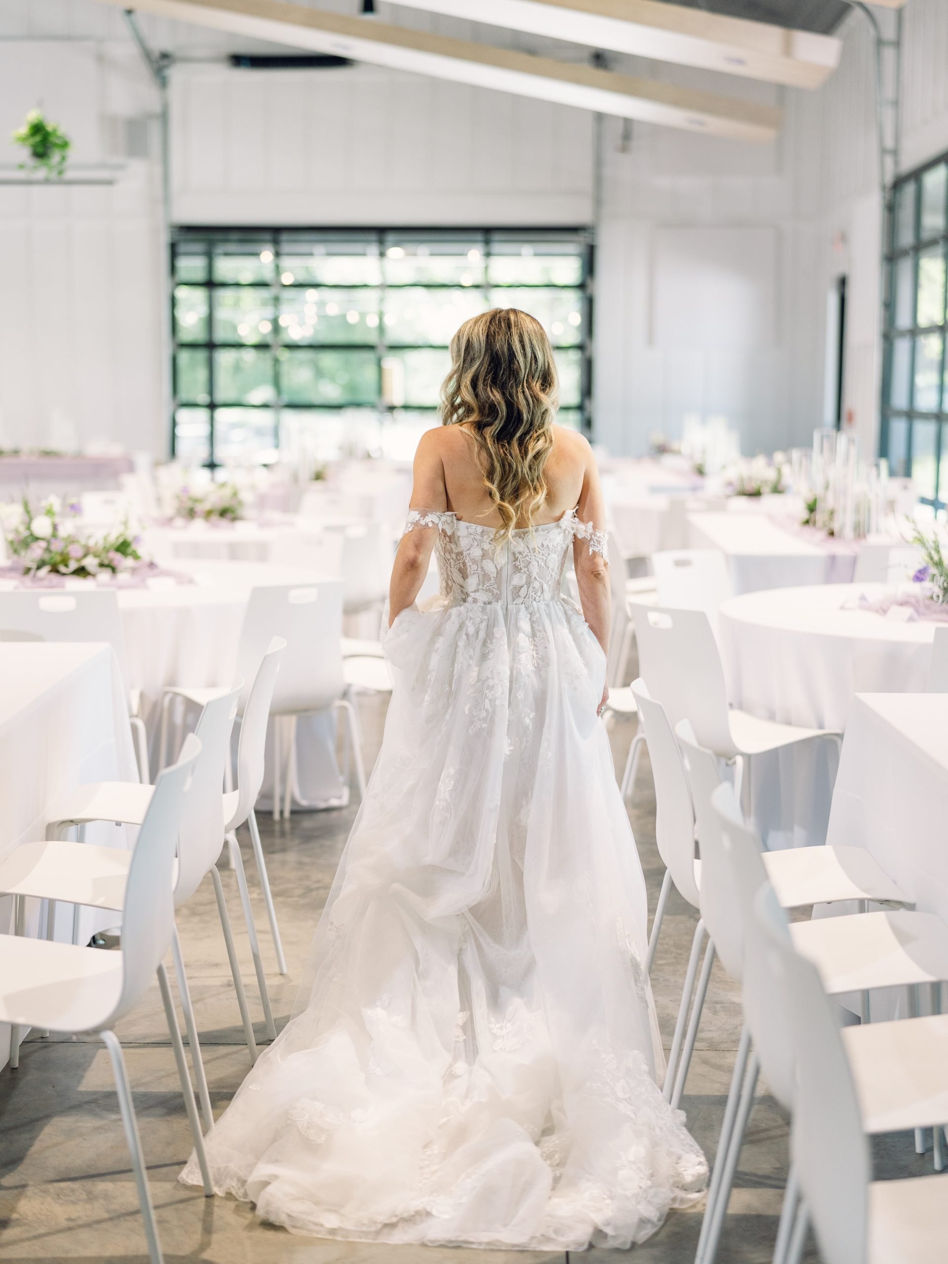 Bride with her back to the camera in empty reception hall with white tables at Retreat 21 near Columbus, Ohio