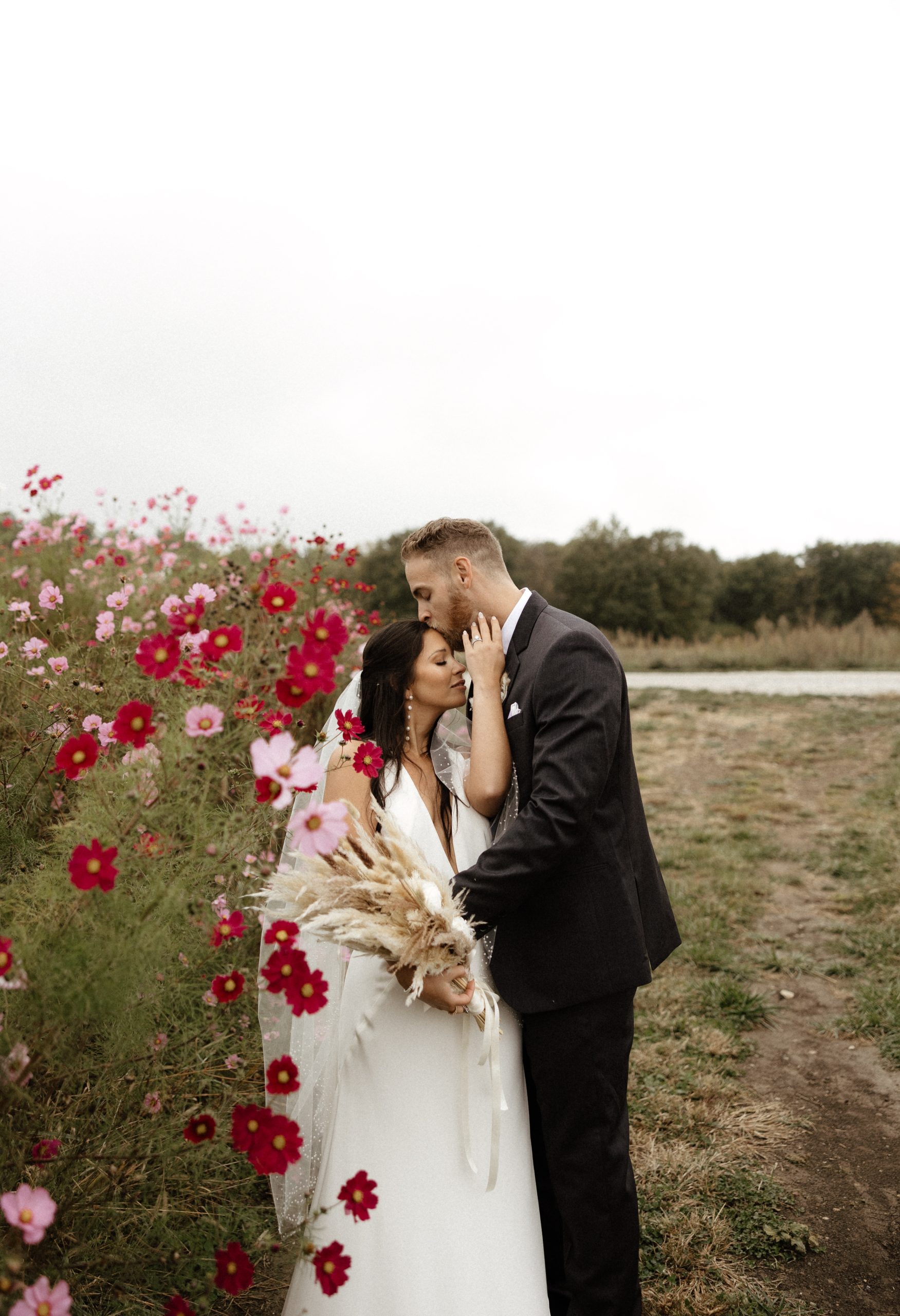 Bride and groom embrace outdoors near a row of pink and red flowers at Retreat 21 near Columbus, Ohio