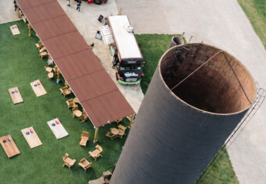 Guests raising their glasses for a toast at a long outdoor reception table at sunset, with food and drinks in front of them